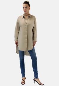 Beige knapp-up skjorta med lång ärm, med en rundad fåll, kombinerad med blå skinny jeans och svarta strap-klackar. Mjuk textur.