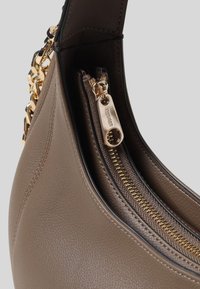 Interieur van een bruine leren handtas met een gouden rits en kettingaccenten, met een gladde textuur en een duidelijk gedefinieerde vorm.