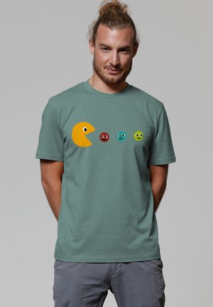 Green cotton t-shirt featuring a large yellow Pac-Man graphic and four colorful ghost characters in red, blue, turquoise, and green.