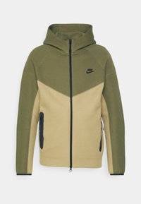 Sudadera con cremallera de Nike en verde oliva y beige en dos tonos, con cremallera y logotipo en negro, capucha y bolsillos laterales con cremallera.