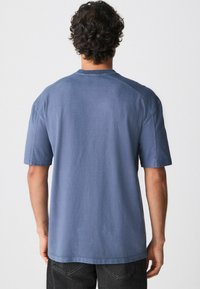 Blaues Baumwoll-T-Shirt mit entspanntem Schnitt, kurzen Ärmeln und Rundhalsausschnitt. Glatte Textur mit sichtbaren Nähten und einem lässigen Design.