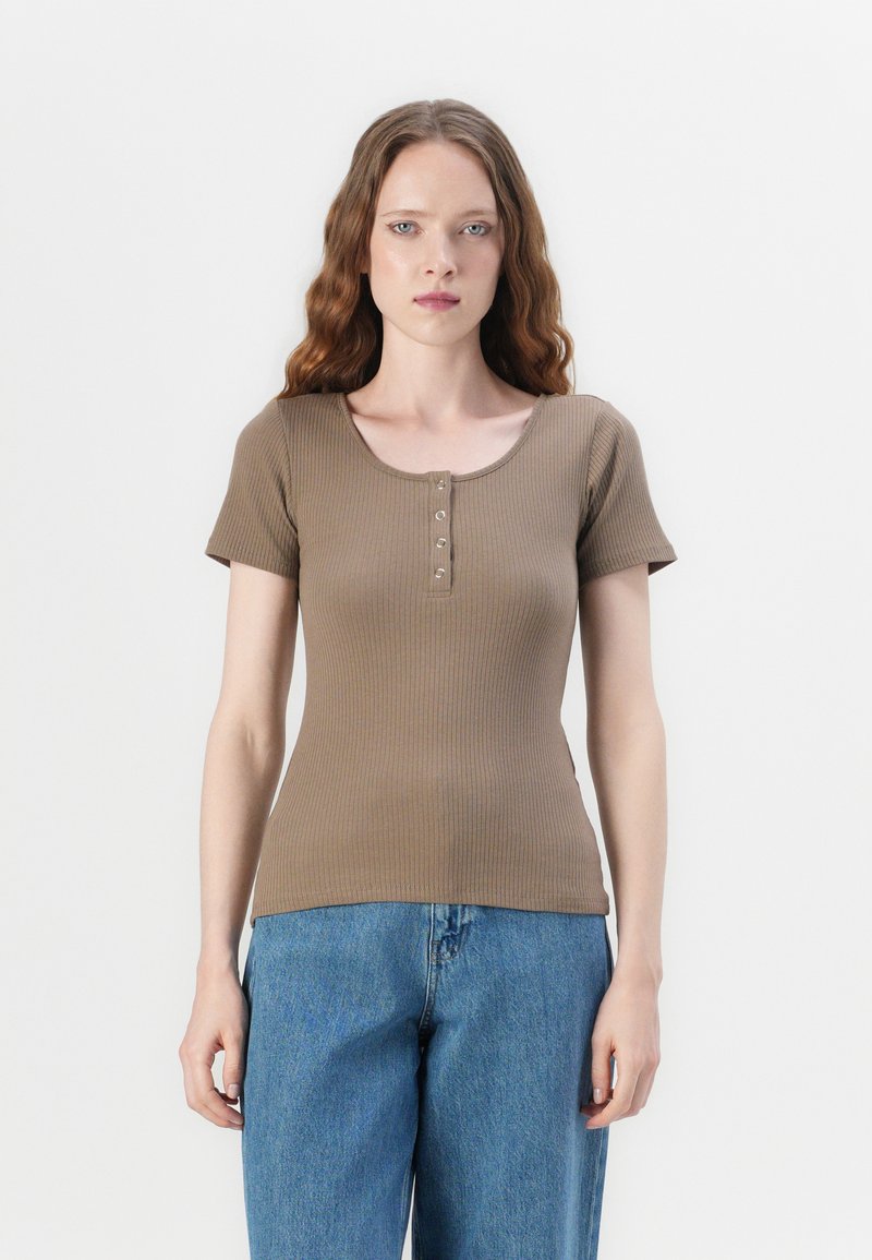 Haut marron à manches courtes côtelé avec un col dégagé, présentant une patte de boutonnage à l'avant et un design ajusté. Porté avec un jean bleu.
