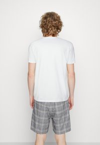 Camiseta de algodón blanca de manga corta, combinada con pantalones cortos de cuadros en tonos de gris, con un corte relajado y textura de algodón.