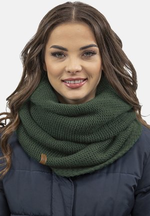Sciarpa lavorata a maglia verde con trama testurizzata, dotata di un'etichetta sulla parte anteriore. Indossata sopra una giacca blu scuro, crea un look stratificato.