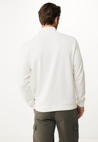 Vit tröja med hög krage, ribbad textur och långa ärmar. Matchad med olivgröna cargobyxor. Inga synliga logotyper eller mönster.