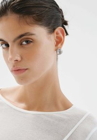 Pendientes de plata en espiral con un diseño texturizado y enrollado. La modelo lleva una blusa blanca de canalé, mostrando los pendientes de manera prominente contra su piel.