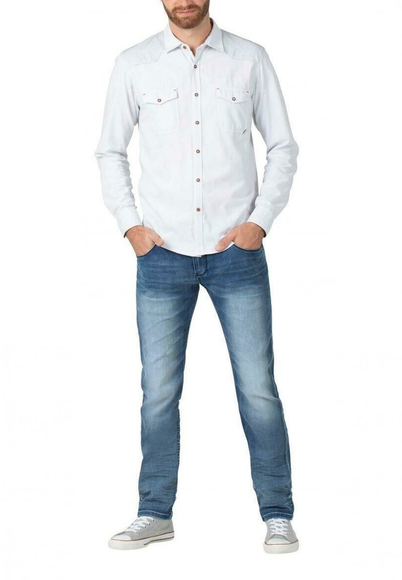 Light blue button-up shirt with two chest pockets and brown buttons, paired with faded blue jeans and white sneakers.