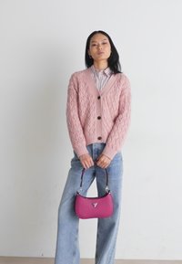 Lyserød strikket cardigan med V-hals, knaplukning, store sorte knapper, parret med højtsiddende lyseblå denimjeans og en lille lyserød håndtaske.