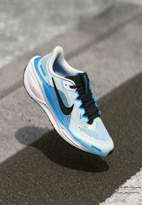 Baskets de course bleu clair avec une tige en mesh respirant, accents noirs et une semelle blanche rembourrée, dotées de surfaces texturées et de lacets.