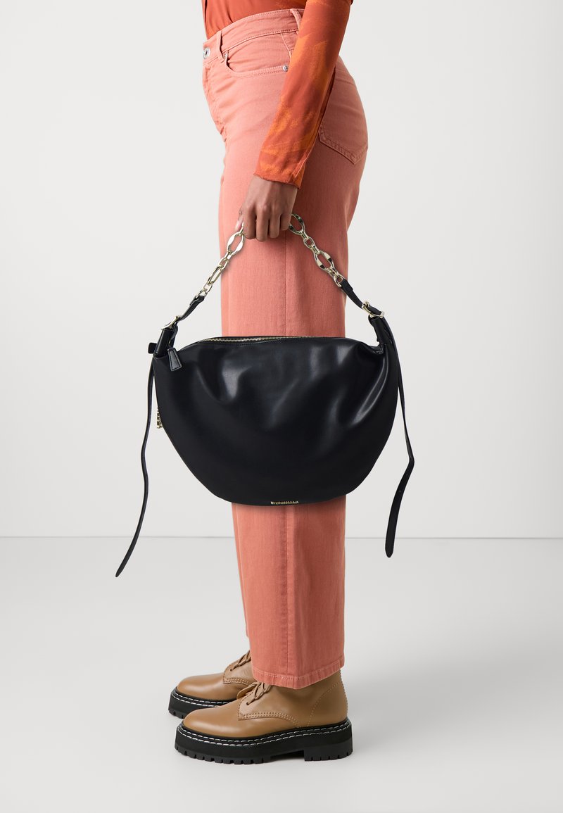 Zwarte leren handtas in een halve maan vorm, met een zilveren kettinghandvat en een ritssluiting. Draag het bij roze broek en tan kleurige veterschoenen.