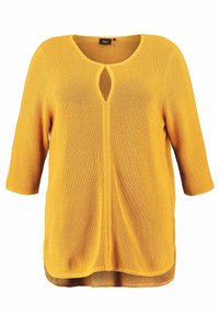 Żółta dzianinowa tunika z okrągłym dekoltem i detalem w kształcie dziurki. Rękawy o długości 3/4 oraz długi, lekko zaokrąglony tył.