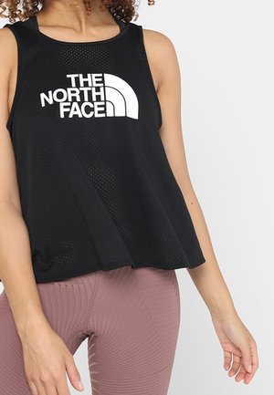 Woman wearing a black sleeveless mesh top with "The North Face" logo and mauve textured leggings, standing with one arm slightly bent.