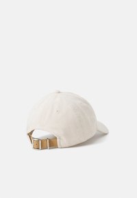 Cappellino da baseball in corduroy beige chiaro con visiera curva, cinturino in pelle regolabile nella parte posteriore e dettaglio a bottone sulla corona.