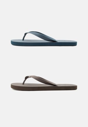 Deux tongs vues de côté avec des semelles texturées et des brides en forme de Y, l'une bleu marine et l'autre marron foncé, sur un fond blanc uni.