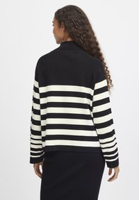 Pull à rayures noir et blanc avec un col haut. Il possède des manches longues et un ourlet droit, fabriqué à partir d'un tissu en tricot doux et texturé.