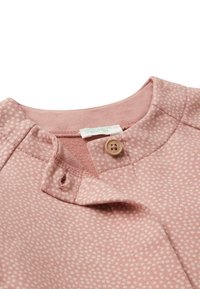 Nahaufnahme eines rosa Hemdkragens mit einem kleinen weißen Punktmuster, einem fest geschlossenen Knopf und einem sichtbaren Markenetikett im Krageninneren.