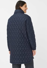 Marineblå quilted lang frakke med et textured diamantmønster, høj krave og elastiske manchetter, designet til varme og komfort i koldere vejr.