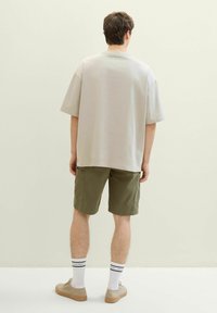 Jasnoszary, luźny t-shirt połączony z oliwkowymi szortami cargo. Stylizacja dopełniona jest białymi skarpetkami i beżowymi trampkami, widziana od tyłu.