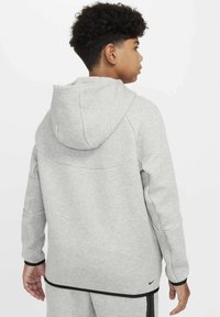 Felpa grigia realizzata in tessuto morbido con cappuccio, caratterizzata da un design semplice e dettagli neri ai polsini e all'orlo. Logo Nike in basso a destra.