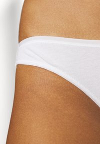 String en coton blanc avec une texture douce, présentant une taille fine et des bords sans coutures, mettant en valeur un design discret.