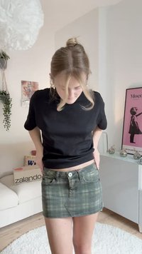 Žalia languota džinsinė mini sijonas su priekinėmis kišenėmis, sagčių užsegimu ir šiek tiek nusidėvėjusiais kraštais. Dėvima su juoda trumpa rankovėmis marškinėliais.