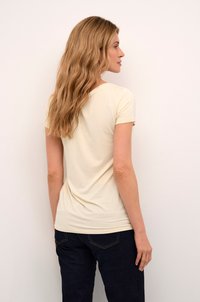 Light beige fitted t-shirt with short sleeves and a rounded neckline, paired with dark blue jeans, displayed from a back view.