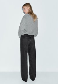 Maglione grigio oversize abbinato a jeans neri a vita alta e a gamba larga. L'outfit presenta una vestibilità casual e rilassata con un design minimalista.
