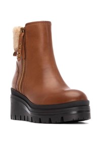 Botín de cuero marrón con un acento esponjoso en la parte superior, cremallera dorada y una suela de plataforma negra gruesa con un dibujo en el piso.