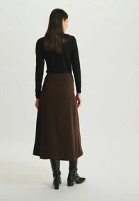 Jupe midi A-line marron en tissu lisse, avec une taille haute et un design fluide, assortie à des bottes noires hautes jusqu'aux genoux.