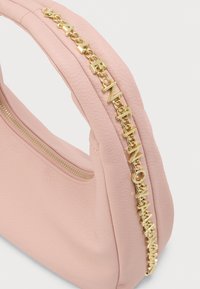 Miękka różowa skórzana torebka z wyściełanym uchwytem ozdobionym złotym łańcuchem z połączonych liter oraz widocznym złotym zamkiem.