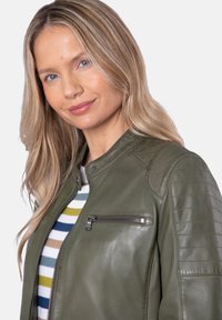 Olive green leather jacket with a zippered chest pocket, ribbed shoulder accents, and a snap collar, worn over a multicolored striped top.