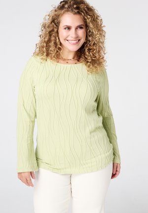 Haut vert clair à manches longues avec un motif texturé ondulé, doté d'un col rond et associé à un pantalon crème.