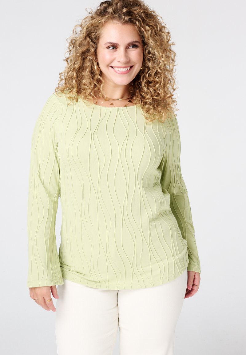 Lichtgroene lange mouwen top met een golvende textuurpatroon, met een ronde halslijn, en gecombineerd met crèmekleurige broek.