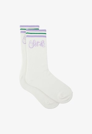 Weiße Crew-Socken mit gerippter Struktur, lila und grüne Streifen oben und lila kursiver Schrift nahe der Manschette.