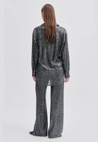 Glänzendes schwarzes Paillettenhemd und passende Hose, locker sitzend mit langen Ärmeln, Seitenschlitzen und glatter Textur.