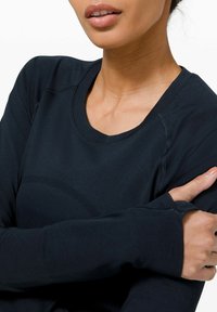 Dunkelgraues Langarm-Sportoberteil mit Rundhalsausschnitt und gerippter Textur. Verfügt über Daumenlöcher in den Bündchen und eine glatte Stoffoberfläche.