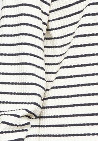 Biała tkanina w granatowe poziome paski, teksturowana drobnym, wypukłym wzorem. Miękki materiał o lekko pomarszczonym wyglądzie.