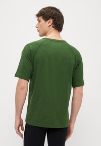 Πράσινο κοντομάνικο μπλουζάκι με χαλαρή εφαρμογή, υφή υφάσματος, στρογγυλεμένο λαιμόκοψη και ραγκλάν μανίκια, εμφανιζόμενο από πίσω.