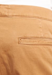 Tan byxor i en smidig bomullsblandning, med en bakficka med en horisontell klaff och kontrasterande sömmar.