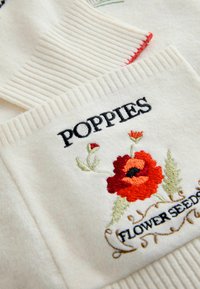 Cream sweater featuring embroidered poppies and "POPPIES FLOWER SEEDS" text. Notable ribbed texture along the edges, with colorful floral details.