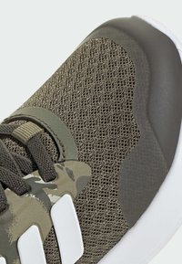 Valkki, jonka yläpinta on oliivinvihreää verkkoa, camomstarviin korostuksia, harmaa kumikanta, valkoinen pohja ja tummanharmaat nauhat. Teksturoidut pinnat näkyvissä.