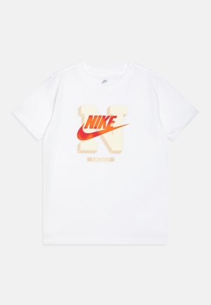 Hvid Nike T-shirt med korte ærmer med et stort beige 3D-bogstav "N" og rødt Nike swoosh-logo midt på, med ordet "Swoosh" nedenunder.