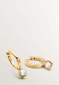 Pendientes de aro dorados con un acabado brillante, que cuentan con un colgante de cristal transparente en un soporte circular, diseño ligero y textura suave.