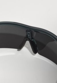 Schwarze Schutzbrille mit geschwungenem Design, glänzender Oberfläche und gummiertem Nasenpolster für Komfort. Die Gläser scheinen getönt zu sein, um UV-Schutz zu bieten.