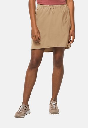 Jupe en tissu léger avec un élastique beige à la taille, avec une coupe décontractée et des poches latérales. Portée avec des chaussures de sport marron clair.