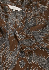 Tissu marron avec motif abstrait noir et blanc en forme de feuille, détail froncé au poignet de la manche et étiquette visible Part Two Copenhagen taille 36.