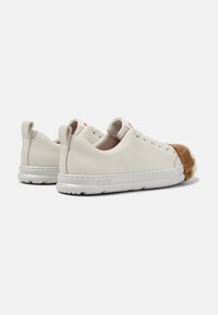 Sneaker beige chiaro con tomaia in pelle liscia, suola in gomma, punta arrotondata e dettaglio della punta di colore marrone in contrasto. Logo rosso sul tallone.