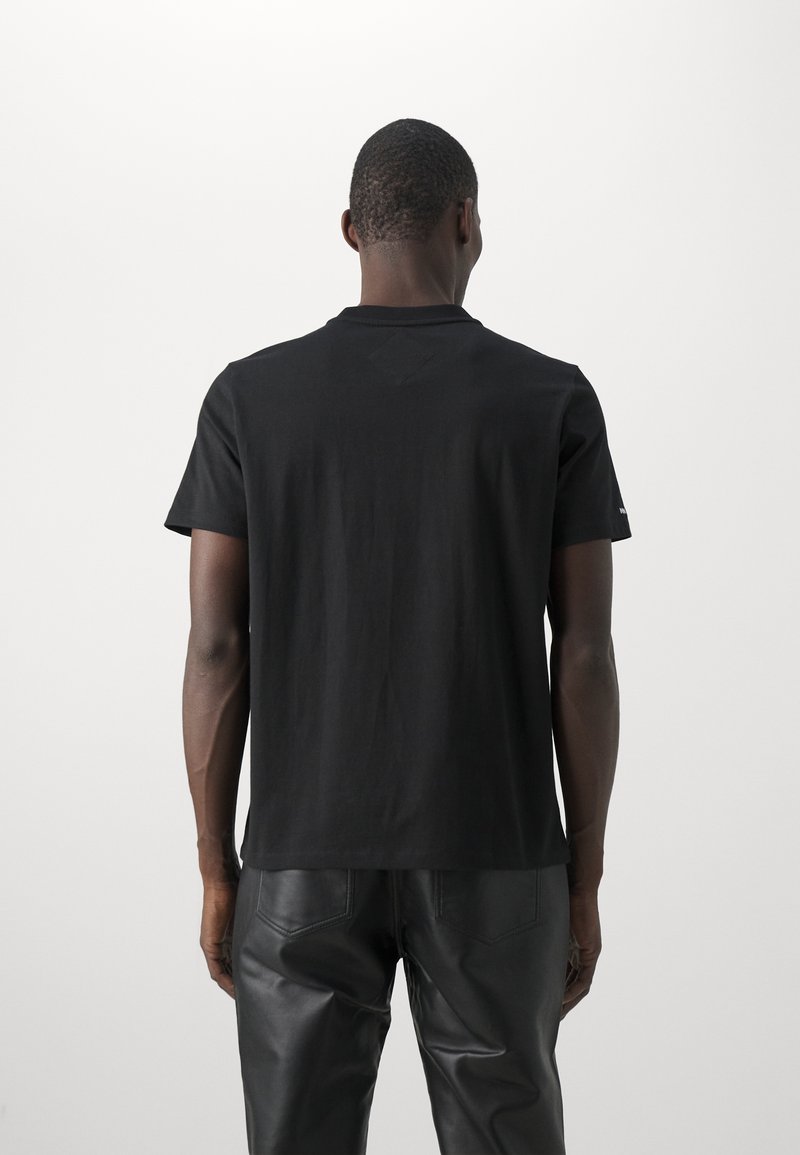 Schwarzes Baumwoll-T-Shirt mit Rundhalsausschnitt und kurzen Ärmeln, mit glatter Textur und schlichtem Design, getragen mit schwarzen Lederhosen.