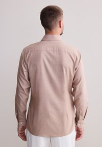 Light brown long-sleeve shirt with a subtle texture, buttoned cuffs, and a standard collar, viewed from the back.