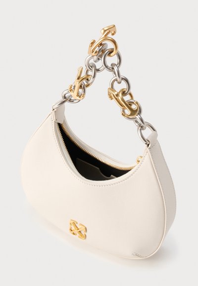Τσάντα ώμου από κρεμ δέρμα με λαβή από χρυσή και ασημένια αλυσίδα, χρυσή λεπτομέρεια με λογότυπο και εν μέρει ανοιχτό φερμουάρ που αποκαλύπτει το μαύρο εσωτερικό.